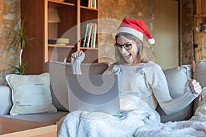 Euphoric woman smiling with arms outstretched glasses and Santa hat sitting on the sofa at home