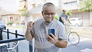 Eureka! cheerful middle-aged caucasian man with beard, firstly celebrating using smartphone on outdoor city street, texting a