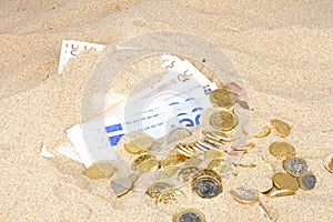 Euro bank notes and coins in the sand