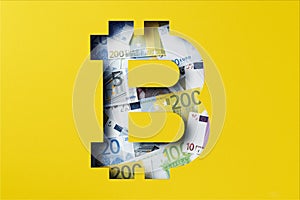 Euro banknote heap under yellow paper cutout, Bitcoin icon