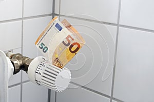 Euro banknote stuck in the thermostat of an heating radiator, rising costs for heat and energy, home finance and money concept,
