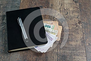 Euro banknotes and fountain pen on wood background. Accounting black book