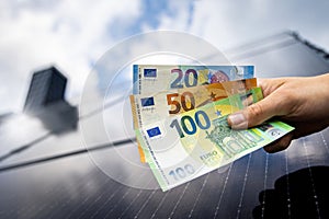 Euro banknotes in a hand with a solar panel roof in the background