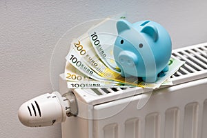 100 and 200 Euro banknotes lying on the radiator together with a small blue piggy bank, The concept of rising costs of heating an