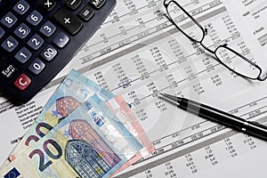 Euro banknotes, pen, calculator and glasses on a mockup balance sheet