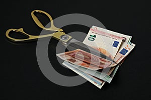 Euro banknotes and scissors on black background