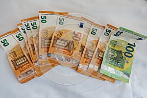 Euro banknotes are spread out on a bed with a white duvet cover