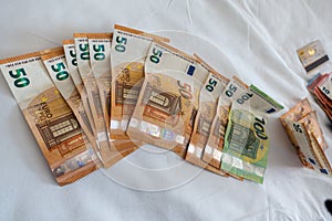 Euro banknotes are spread out on a bed with a white duvet cover