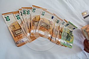 Euro banknotes are spread out on a bed with a white duvet cover