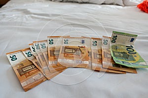 Euro banknotes are spread out on a bed with a white duvet cover