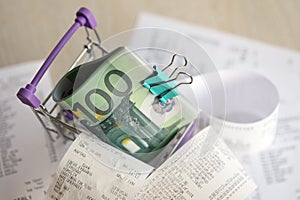 Euro bills bunch in shopping trolley surrounded by many paper receipts