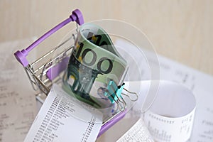 Euro bills bunch in shopping trolley surrounded by many paper receipts