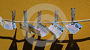 Euro bills hanging on a rope on clothespins and flutter. Money sways in the wind on the background of yellow wall