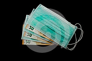 Euro Bills laying between medical masks, concept of increasing costs for protection of virus isolated on black background