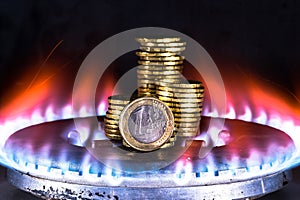 A euro coin closeup along with a row of yellow coins on a gas burner against a blue flame of natural gas on a dark