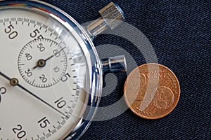 Euro coin with a denomination of 2 euro cents and stopwatch on black denim backdrop - business background