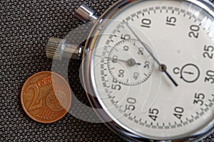 Euro coin with a denomination of 2 euro cents and stopwatch on brown denim backdrop - business background