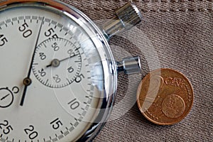 Euro coin with a denomination of 2 euro cents and stopwatch on old beige jeans backdrop - business background