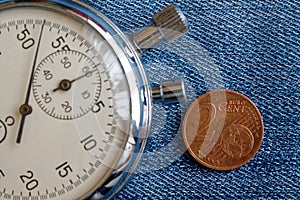 Euro coin with a denomination of 2 euro cents and stopwatch on worn blue denim backdrop - business background