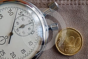 Euro coin with a denomination of 20 euro cents and stopwatch on old beige jeans backdrop - business background