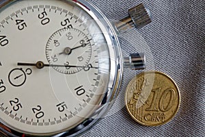 Euro coin with a denomination of 10 euro cents and stopwatch on gray denim backdrop - business background