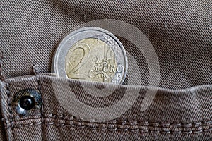 Euro coin with a denomination of 2 euro in the pocket of vintage gray denim jeans