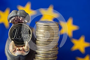 Euro coin in mouth of hippo figurine, EU flag