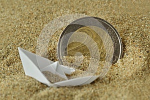 Euro coin and paper boat sinking in the sand - Concept of immigration