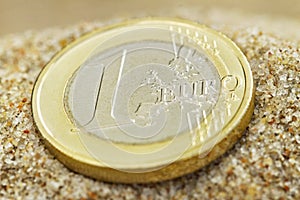 Euro coin on sand.