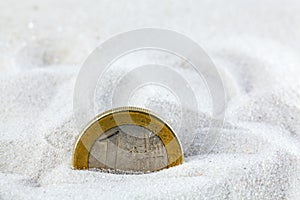 Euro coin in sand.