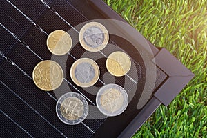 The euro coins on electrical solar panel placed on the green grass.