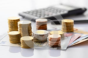 Euro coins in pile on Euro banknotes with calculator and pen, for background