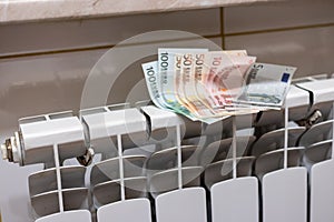 Euro money banknotes on heating radiator battery with temperature regulator at home