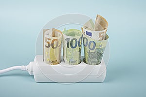 Euro money banknotes plugged in power strip extension cord on light blue background. Electricity prices increasing every