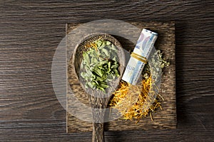 Euro money roll and dry herbal remedies on dark wooden plate and spoon.