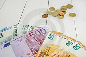 Euro notes and coins on a white, wooden background.