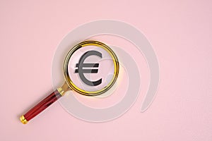 Euro symbol under magnifying glass, on pink background