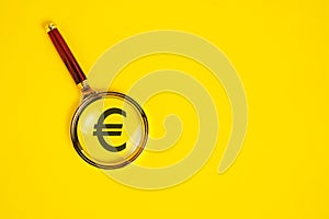 Euro symbol under magnifying glass, on yellow background