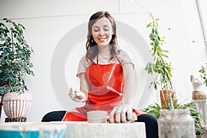 European artist girl making clay dishes on potter wheel, happy and smiling. Concept of love for work, craft