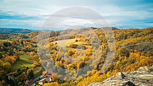European autumn rural landscape,valley with fields,winding road among hills covered with colorful fall forest,cloudy sky