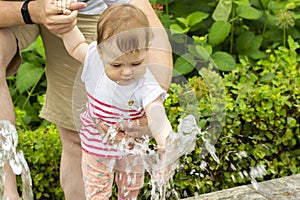 European baby girl playing with jets of water in a fountain. Baby wets her hands in the fountain. Caucasian girl playing with