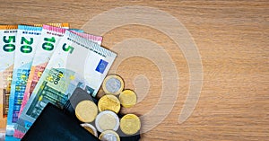 European banknotes and coins in black leather wallet on wooden background. Euro money.