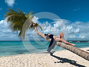 European beautiful happy dark haired girl with sunglasses in bikini and blue pareo is lying on coconut palm on the white sand