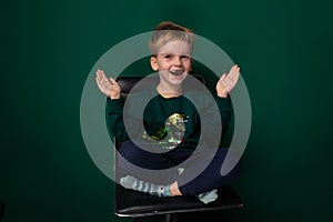 European blond boy smiling cutely sitting on a chair on a green background