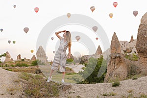 European blonde girl standing with hot air balloons and rocks on background in Capadocia.