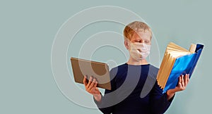 European boy in a white medical mask holding a tablet in one hand and an open book in the other