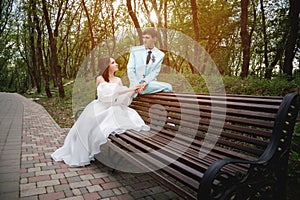 European bride and groom are sitting on a park bench. Newlyweds admiring each other while walking through a green summer