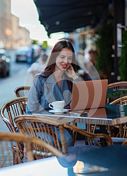 European business woman is working with laptop outdoors during coffee break, plans presentation, is focused on documents