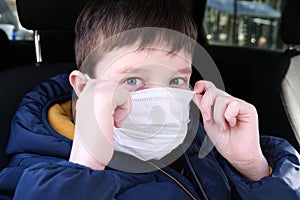 A european caucasian teenage boy in car putting on white protective surgical medical face mask as a protection against virus