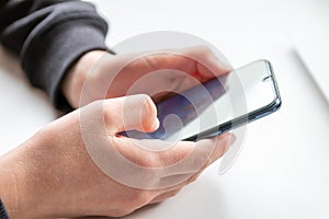 European child hands holding black smartphone with fingers and black screen on white desk infront of white notebook at school